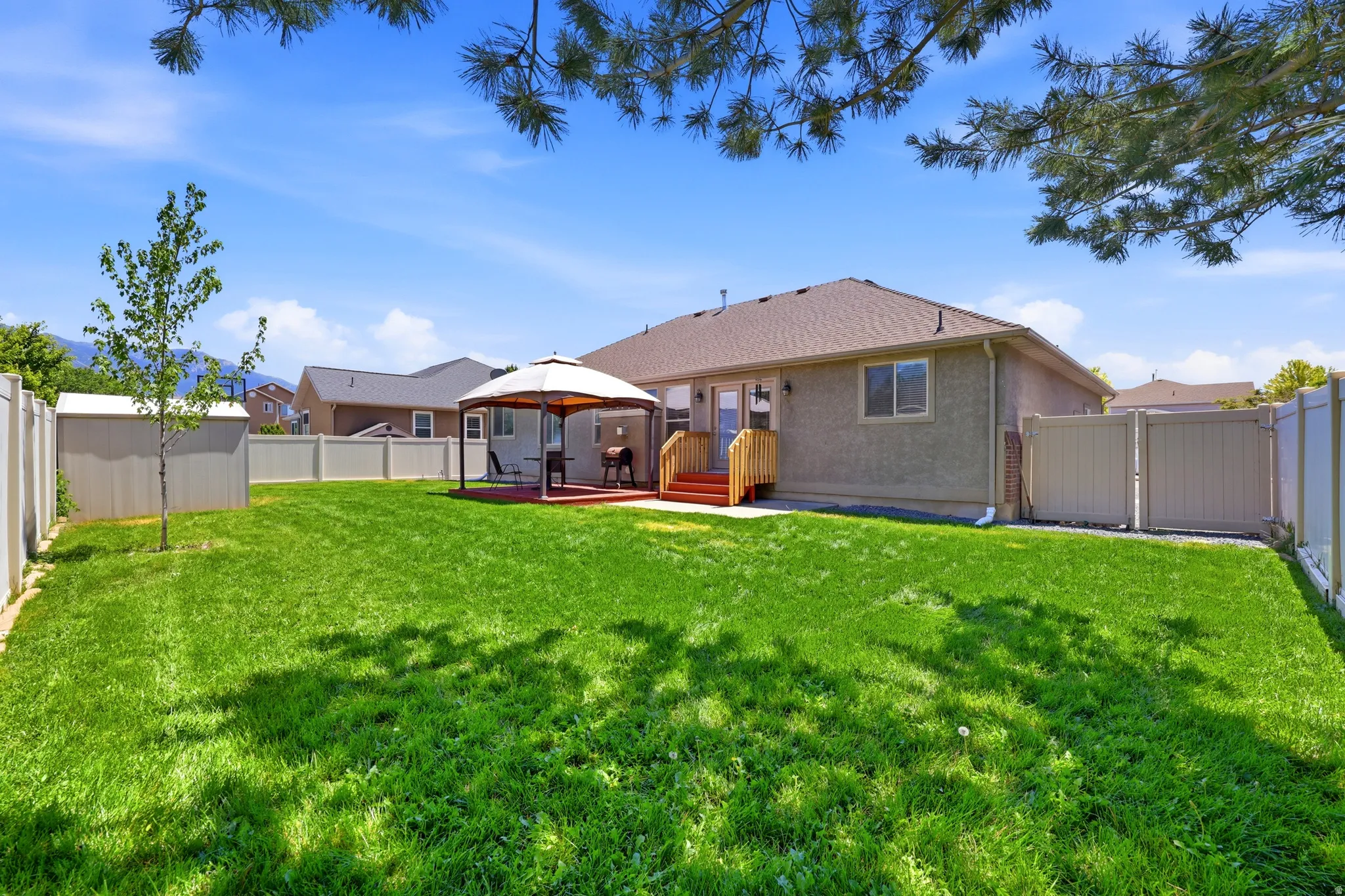 Expansive backyard featuring a large green lawn, covered patio area, storage shed, full privacy fencing, and a stucco exterior on the home