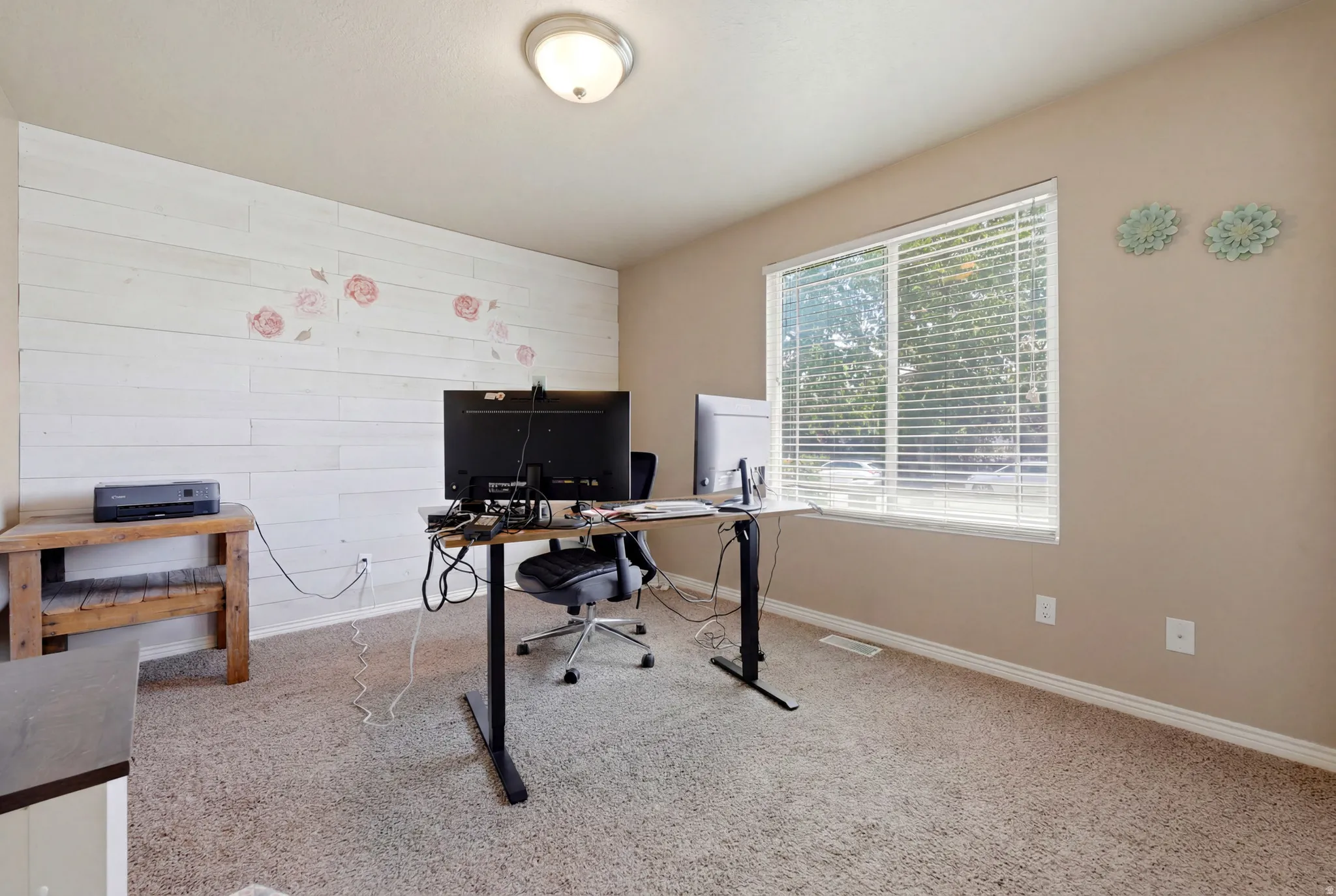 Room featuring a shiplap accent wall, light tan carpeting, and a double window with horizontal blinds