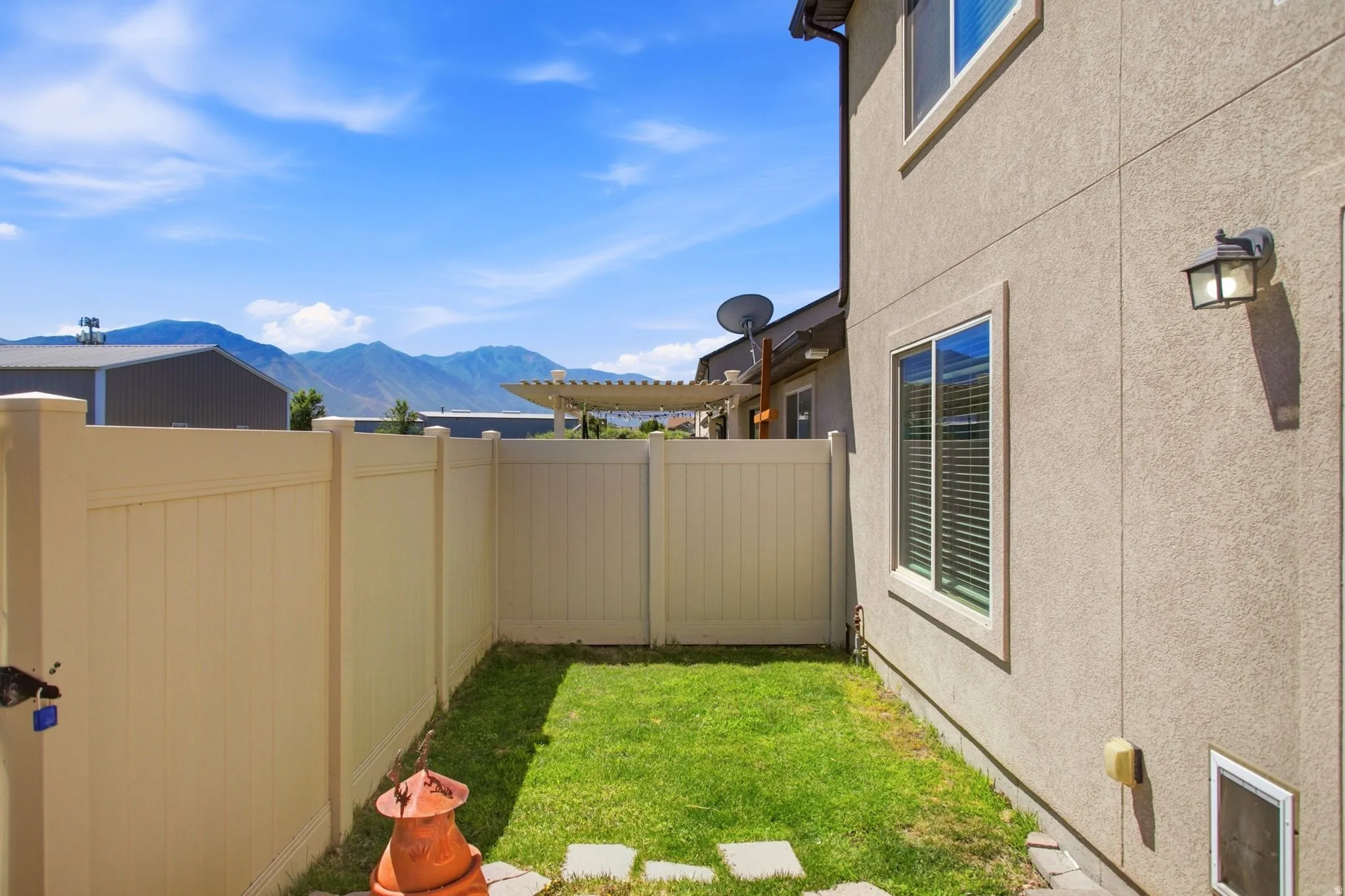 Private side yard featuring a manicured lawn, stone paver pathway, and light-toned vinyl fencing