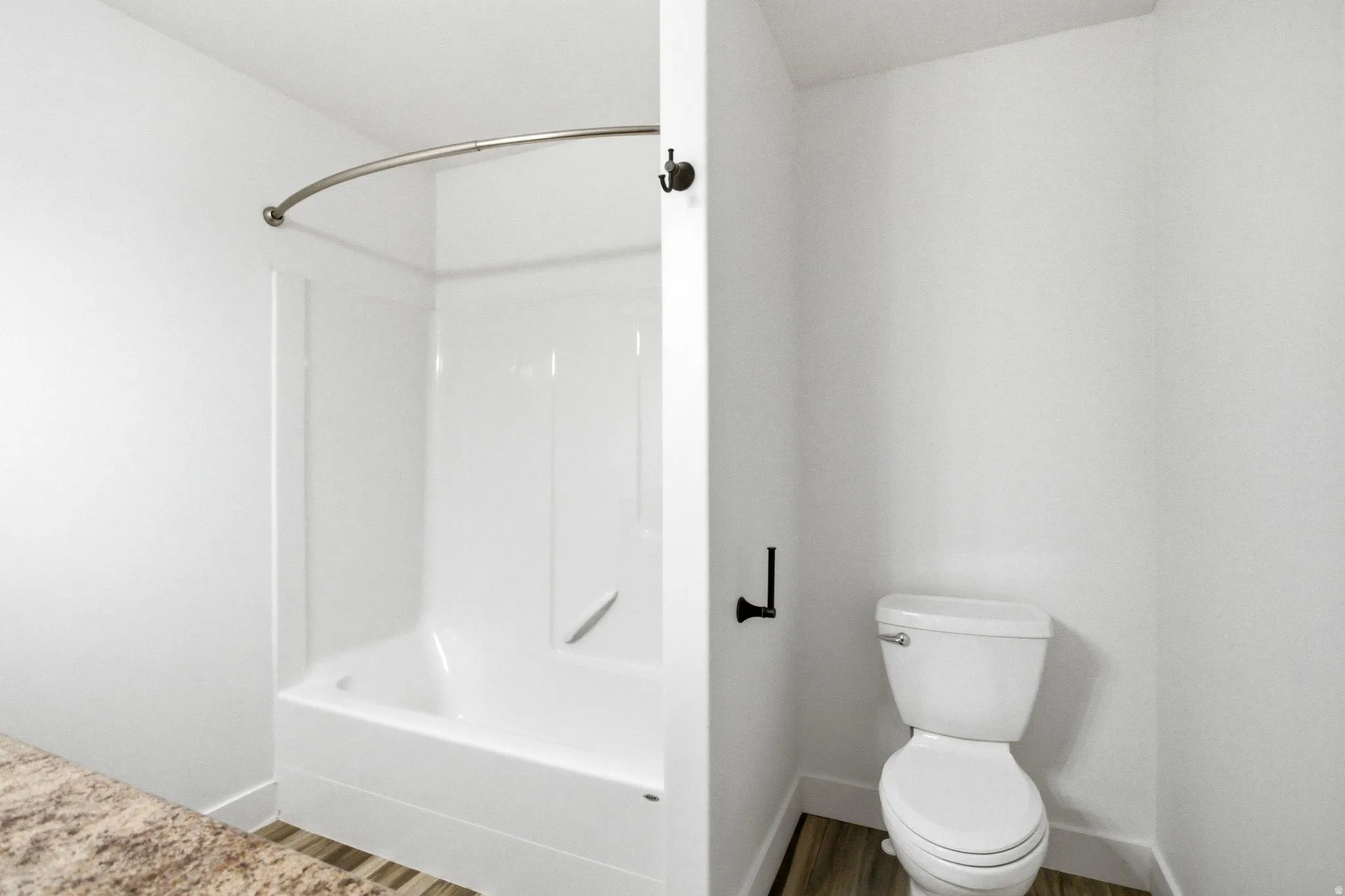 Bathroom featuring a white tub-shower combination with a curved shower rod, white toilet, wood-finish flooring, and a stone-look countertop