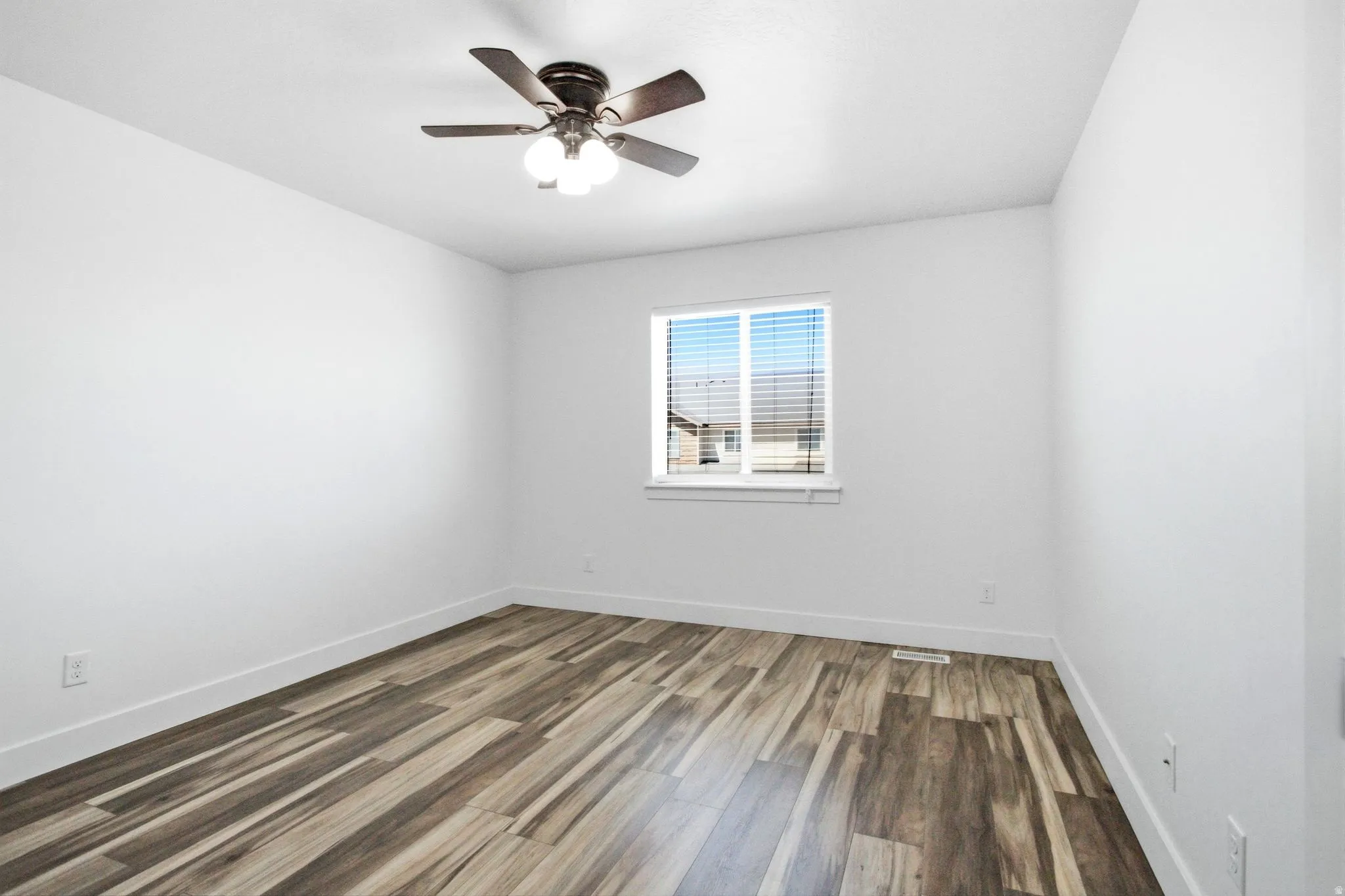Interior room featuring wood-finish flooring, white walls, and a multi-pane window with blinds