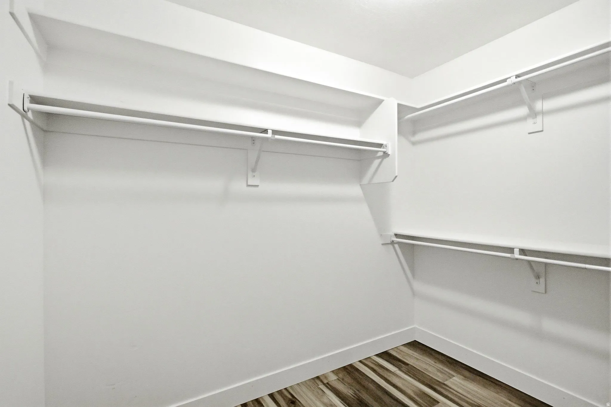 Walk-in closet featuring white shelving, hanging rods, white baseboards, and wood-finish flooring