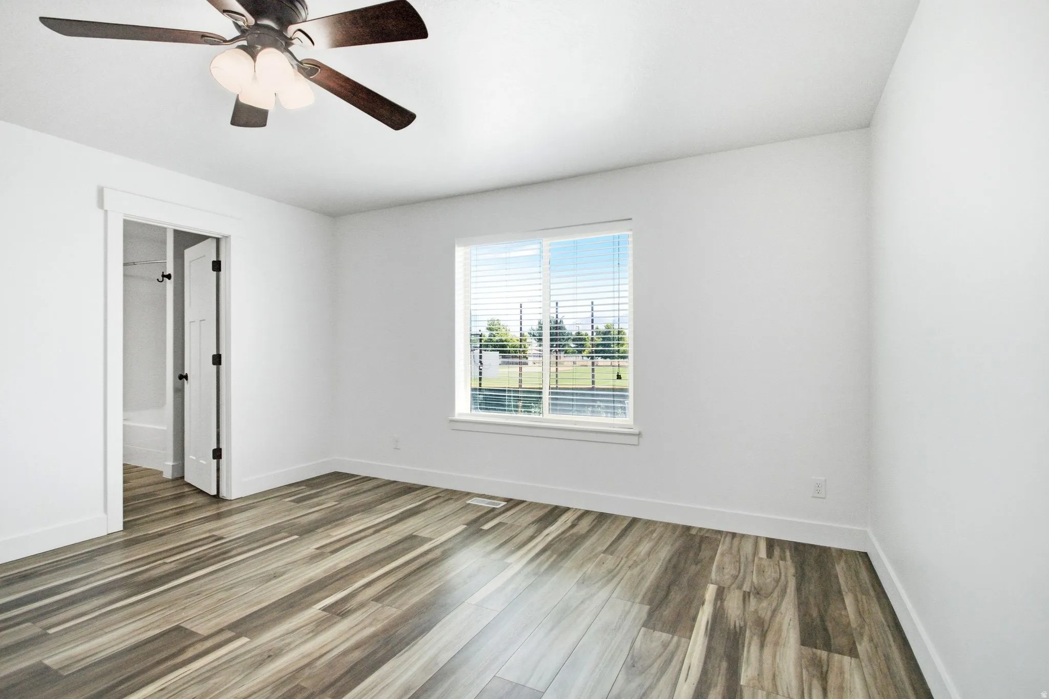 Bright interior space featuring wood-finish flooring, white walls, and a ceiling fan with integrated lighting
