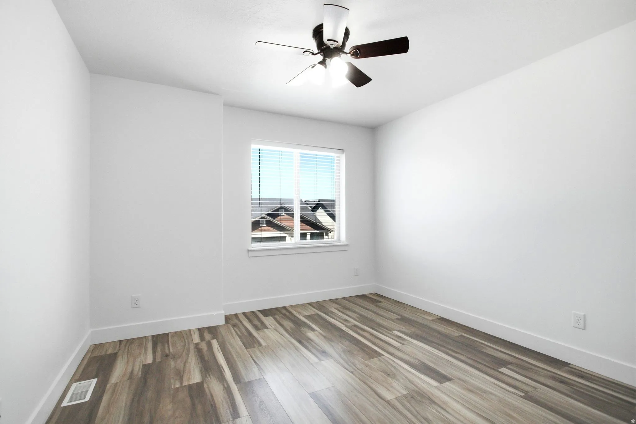Bright room featuring wood-finish flooring, a ceiling fan with integrated lighting, and a window with blinds