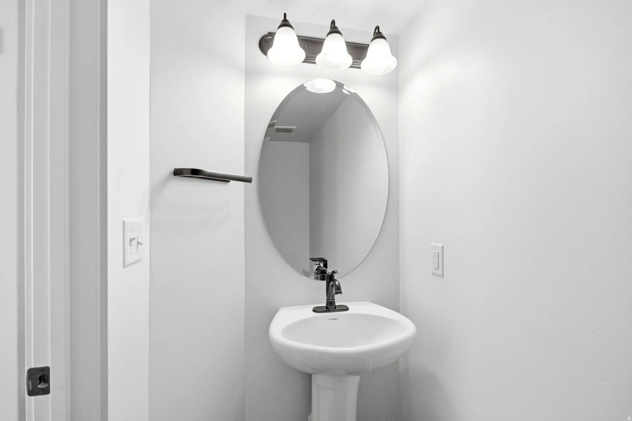 Pedestal sink with a dark bronze faucet, illuminated by a three-light vanity fixture