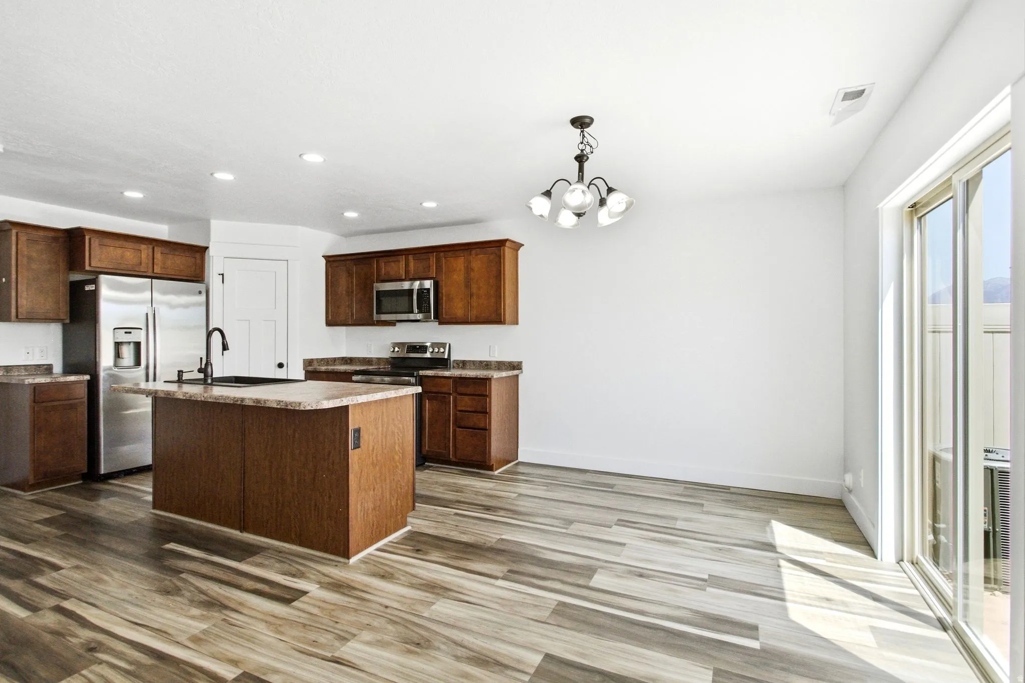 Open-concept kitchen and dining area featuring wood-finish flooring, rich wood cabinetry, stainless steel appliances, a central island, and a sliding glass door