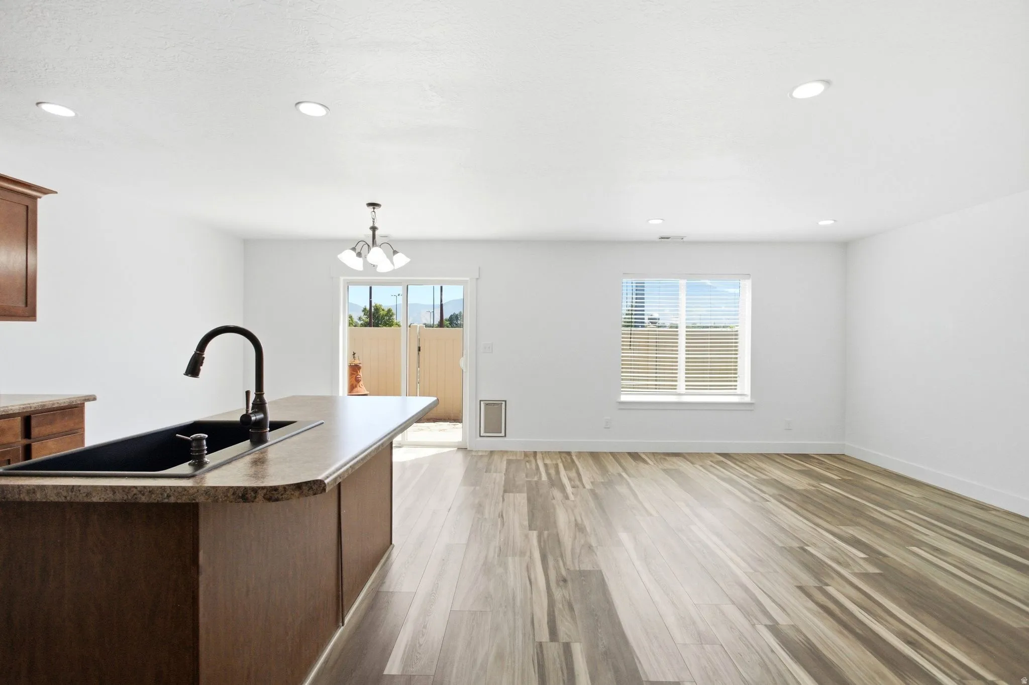 Open concept living space featuring wood-finish flooring, recessed lighting, and a kitchen island with an integrated black sink and matte black faucet