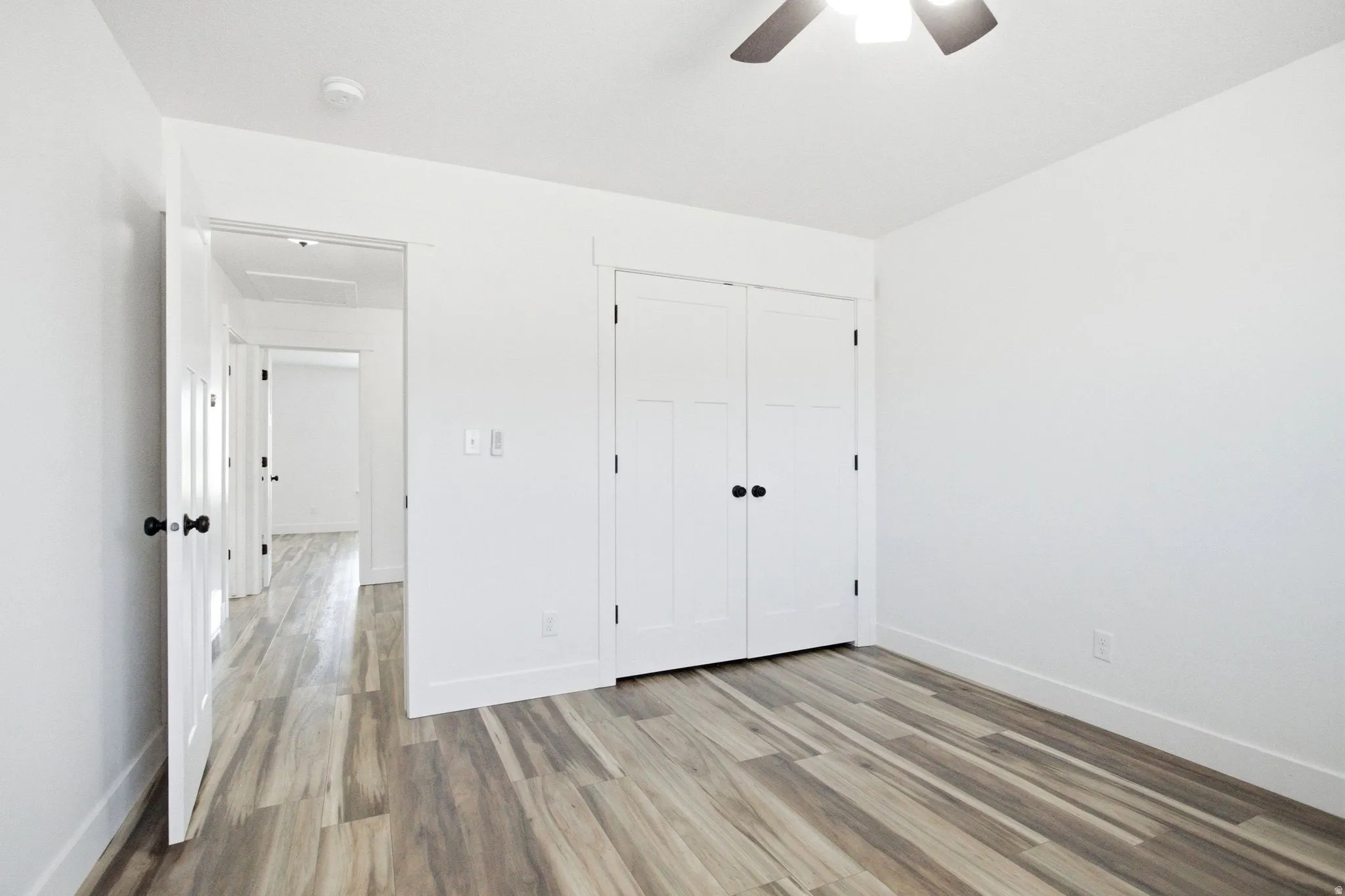 Room featuring wood-finish flooring, white walls, and a ceiling fan