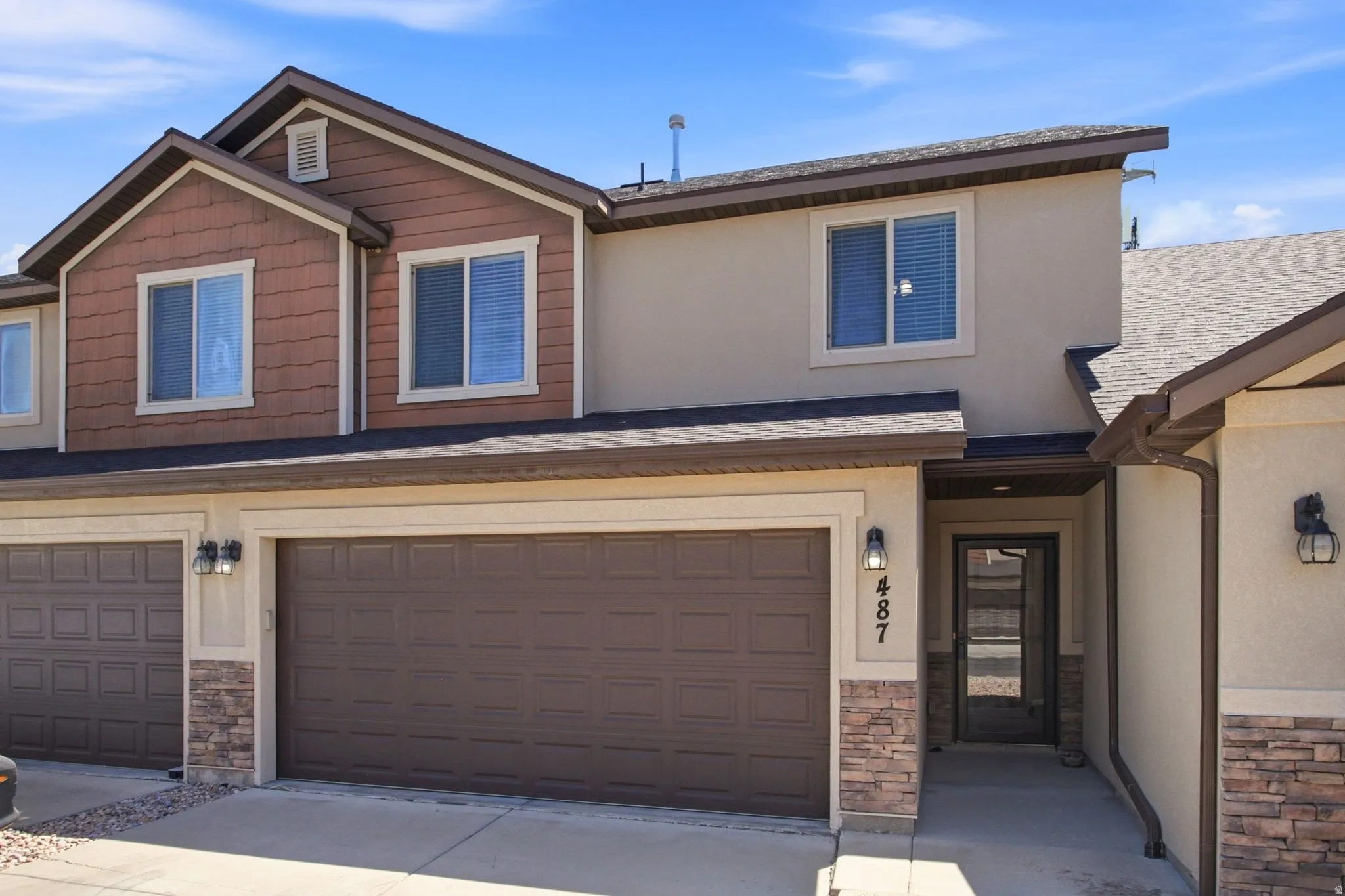 Multi-level townhouse exterior featuring a two-car garage, stacked stone accents, and a covered entry