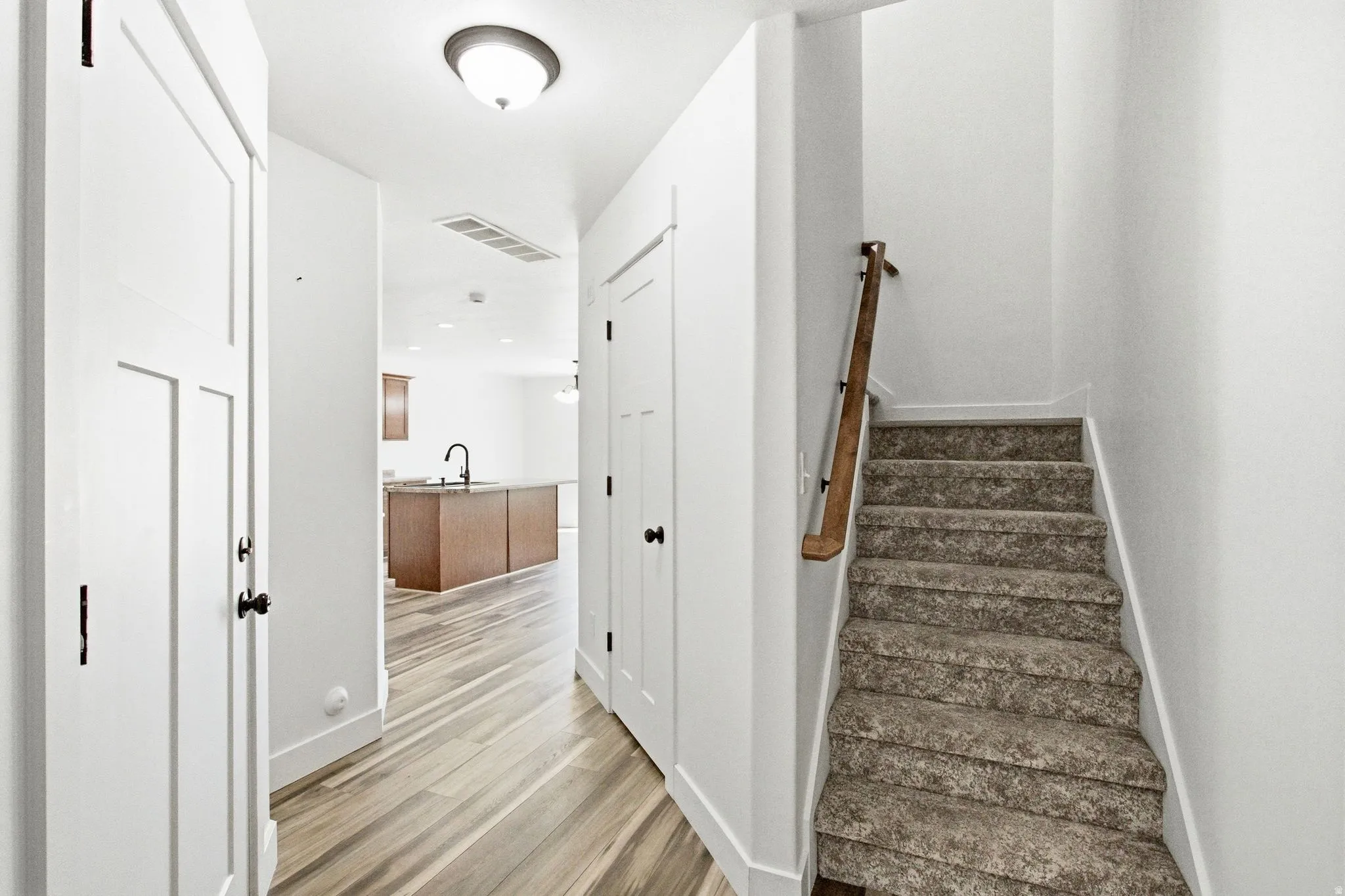Entryway with wood-finish flooring, white paneled doors with black hardware, and a staircase featuring carpeted treads and a wood handrail