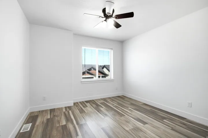 Bright room featuring wood-finish flooring, a ceiling fan with integrated lighting, and a window with blinds