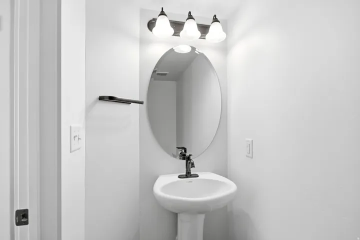 Pedestal sink with a dark bronze faucet, illuminated by a three-light vanity fixture