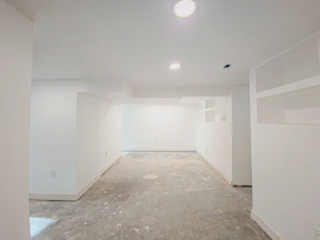 Unfinished concrete flooring, white painted walls, recessed lighting, and built-in shelving new carpet on the way!