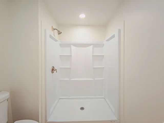 White shower stall with built-in shelving, a brushed nickel shower head, and matching faucet