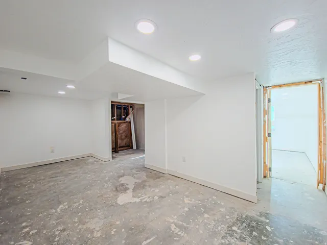 Recessed lighting illuminates the open space with unfinished concrete flooring, new carpet on the way! Laundry room in background.