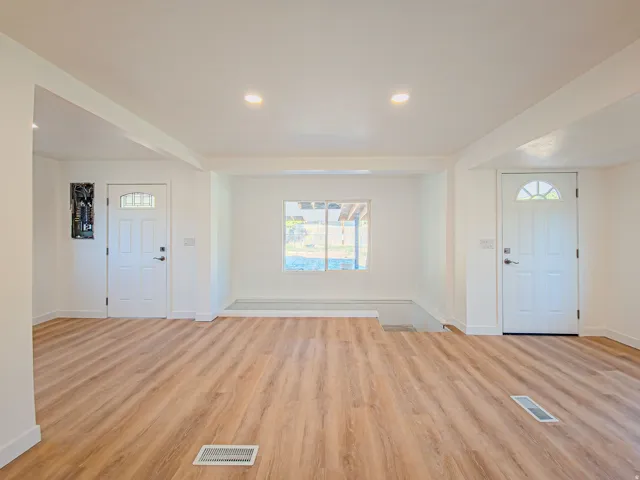 Recessed ceiling lighting, wood-finish flooring, white doors with arched lites, white walls, and a large window with vaulted ceiling over stairs and plenty of natural light