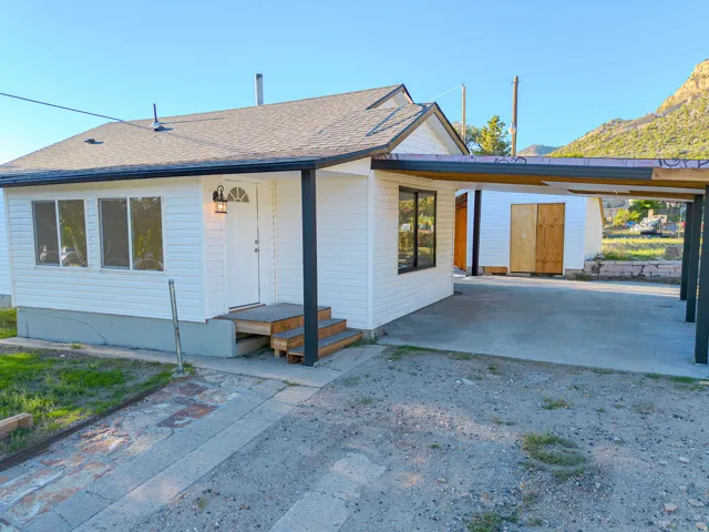 White siding exterior with a dark-shingle roof, featuring a covered carport and a front porch with wooden steps