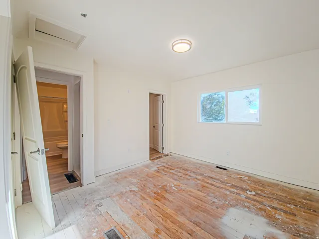 Room featuring wood plank flooring, white walls, two windows, and an overhead light fixture, new carpet on the way!