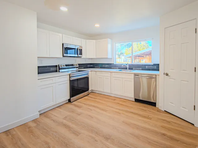 White cabinetry with stainless steel appliances, wood-finish flooring, and a dark tile backsplash