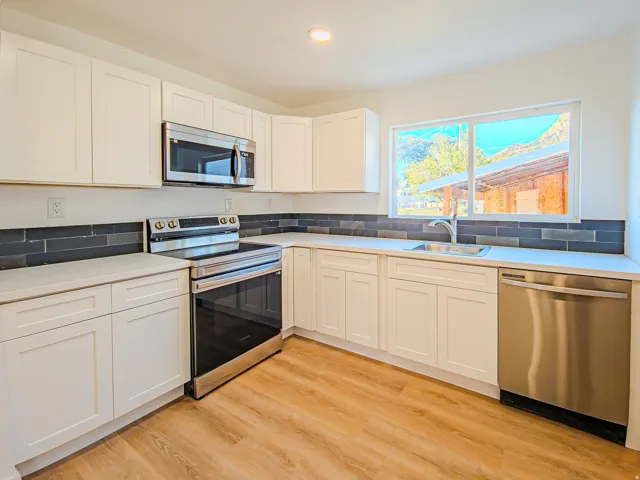 Kitchen featuring white cabinetry, light-toned countertops, a dark subway tile backsplash, stainless steel appliances, and wood-finish flooring