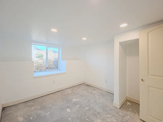 Large windows with lots of natural light. Recessed ceiling lighting, white painted walls, window with white trim, white paneled door, and concrete flooring, new carpet on the way!