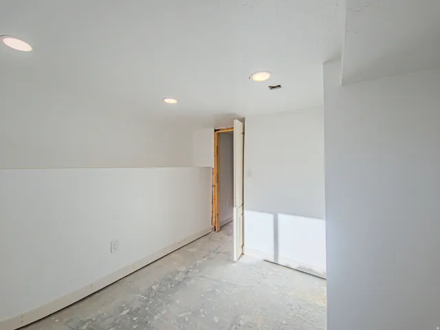 Recessed ceiling lighting, white painted walls, and an open doorway, new carpet on the way!
