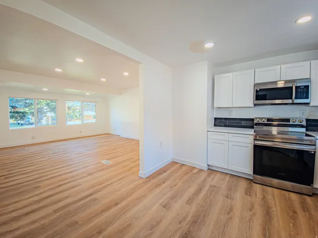 Contemporary kitchen with white cabinetry, stainless steel appliances, dark tile backsplash, and light countertops