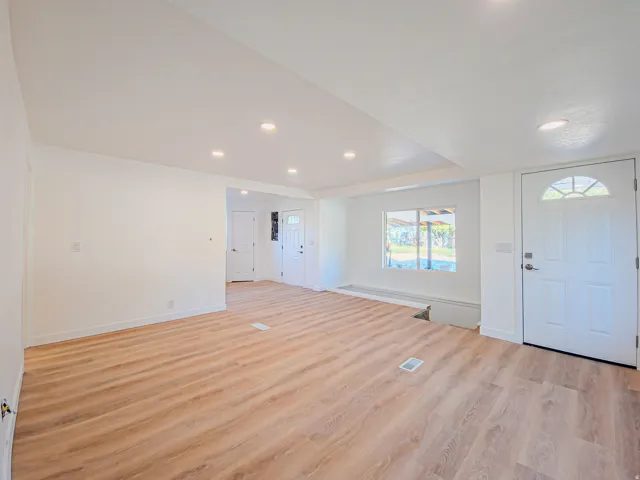 Spacious living room featuring wood-finish flooring, recessed lighting, and a white paneled entry door with an arched transom