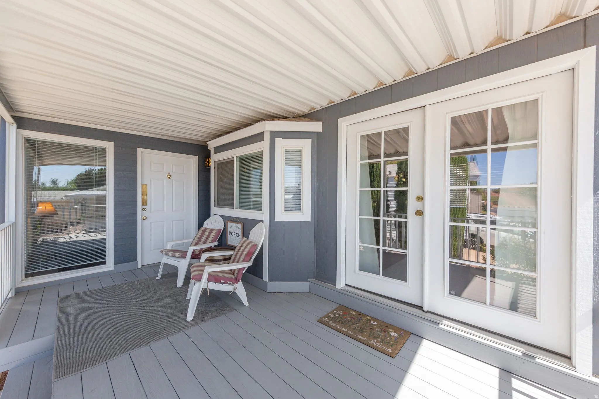 Covered porch featuring a gray wood-finish deck, white railing, and paneled siding
