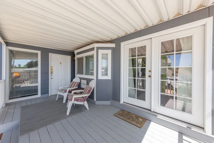 Covered porch featuring a gray wood-finish deck, white railing, and paneled siding