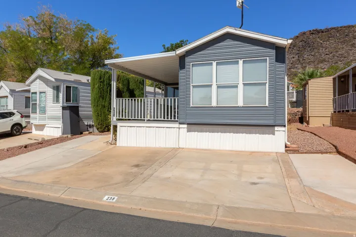 Exterior featuring gray horizontal siding, white trim, a covered porch, an asphalt driveway, and a concrete parking pad