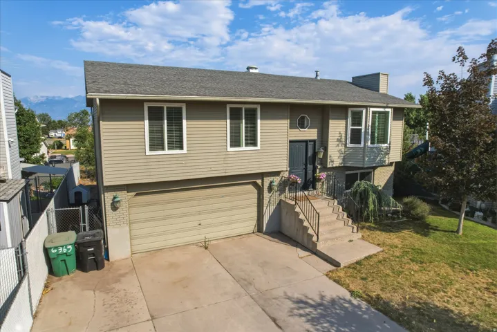 Split-level residence featuring tan horizontal siding, a two-car garage, and a concrete driveway