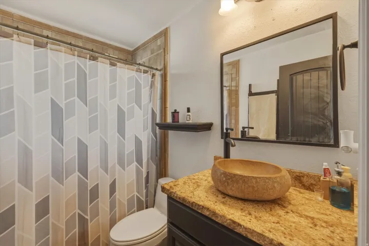 Modern bathroom featuring a stone vessel sink, granite countertop, dark wood vanity with a black faucet, and a large framed mirror