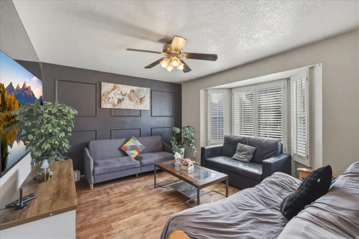 Living area featuring wood-finish flooring, a decorative accent wall, and a ceiling fan with integrated lighting