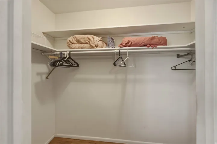Corner closet featuring white shelving and hanging rods