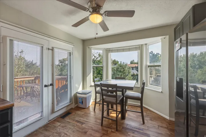 Kitchen dining area featuring wood-finish flooring, a bay window, and double French doors opening to an outdoor deck