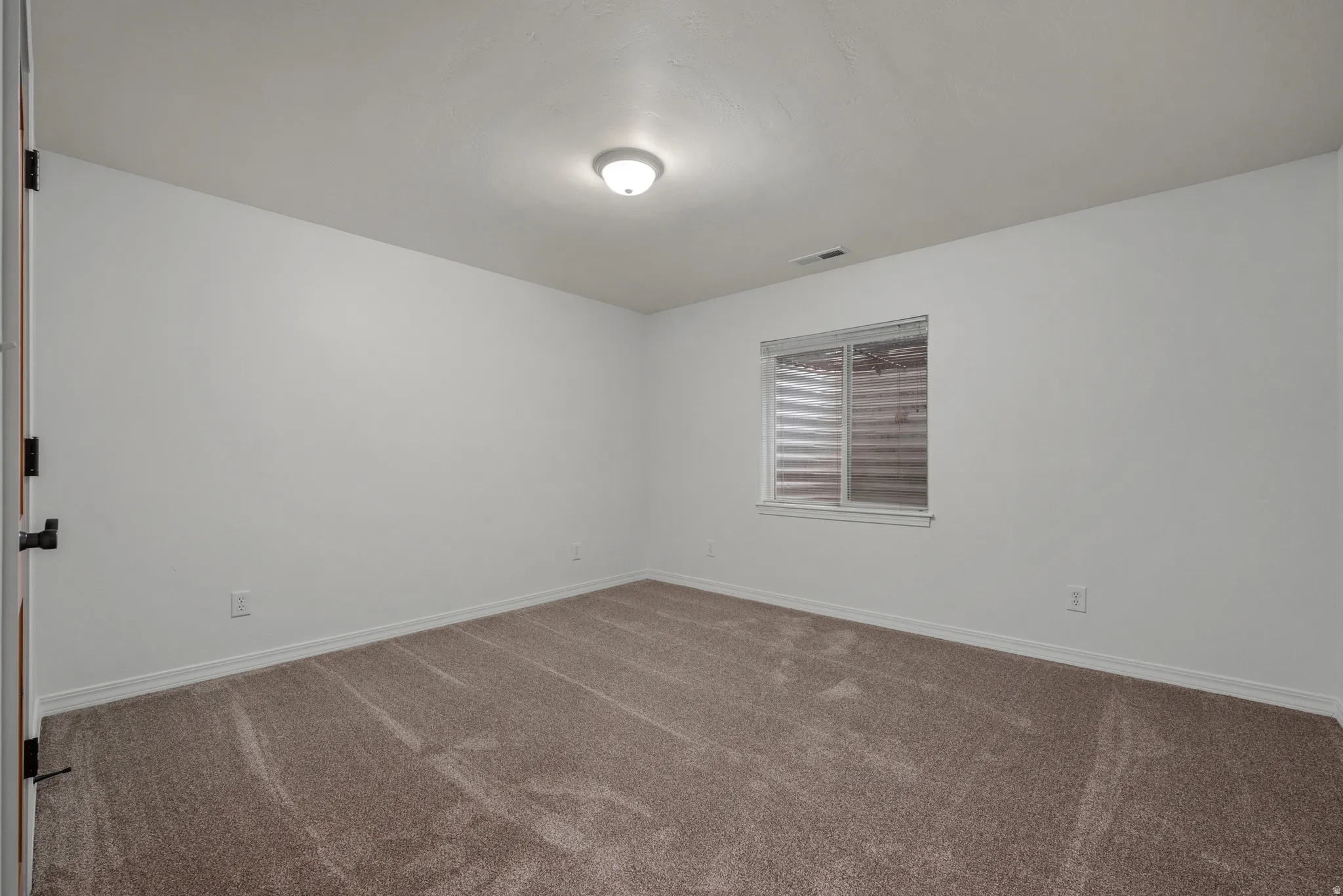 Room featuring neutral tone carpeting, white walls, a single window with blinds, and a flush mount ceiling light fixture