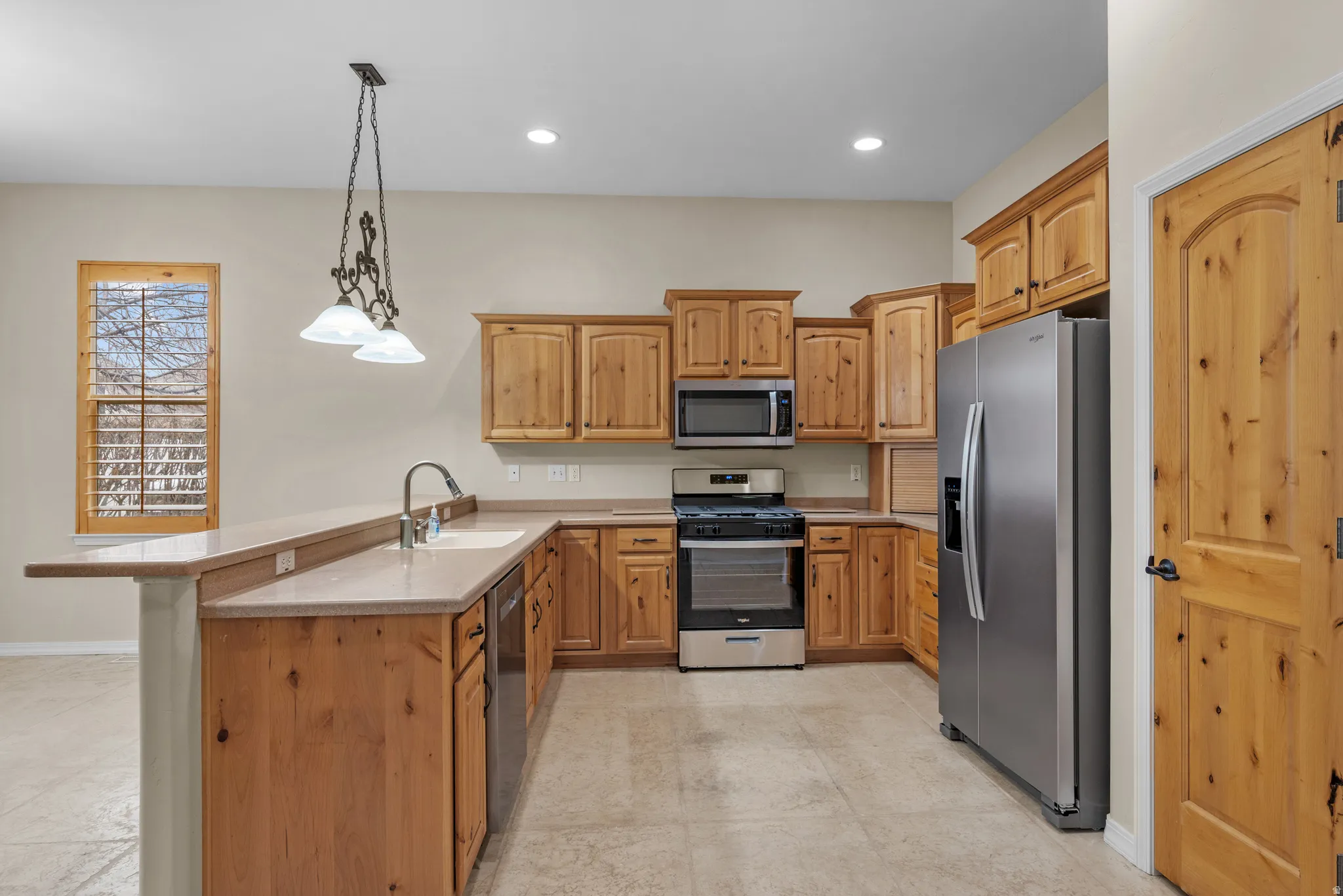 Kitchen featuring natural wood cabinetry, stainless steel appliances, a stone-finish countertop, and a breakfast bar
