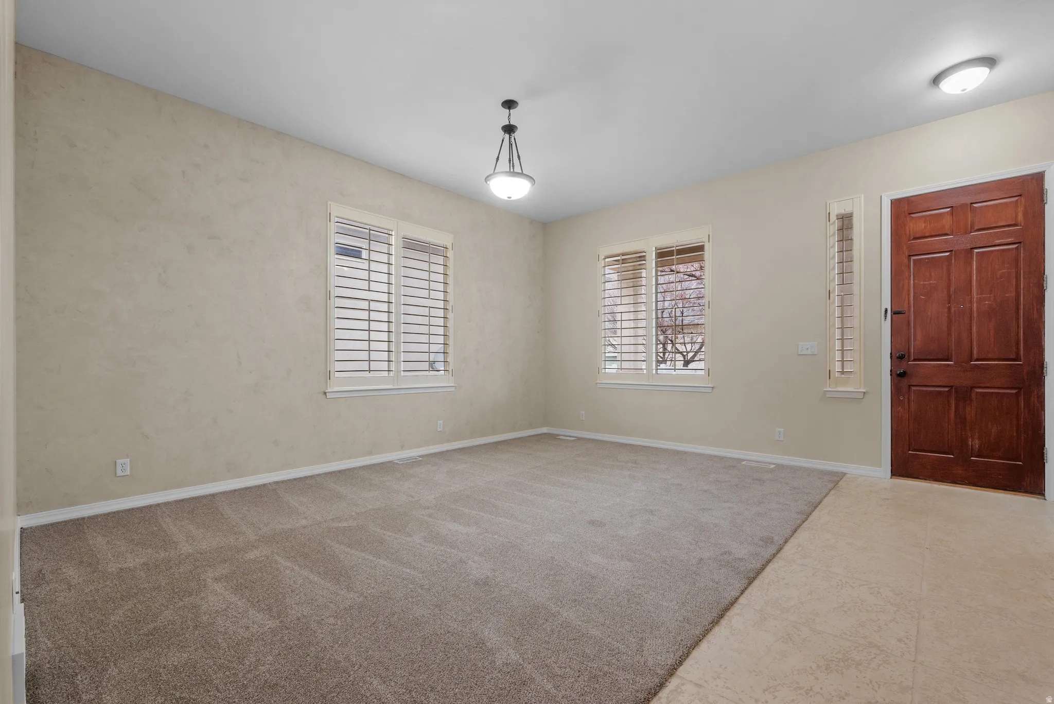 Spacious room featuring neutral carpeting, light-toned walls, and multiple windows with plantation shutters