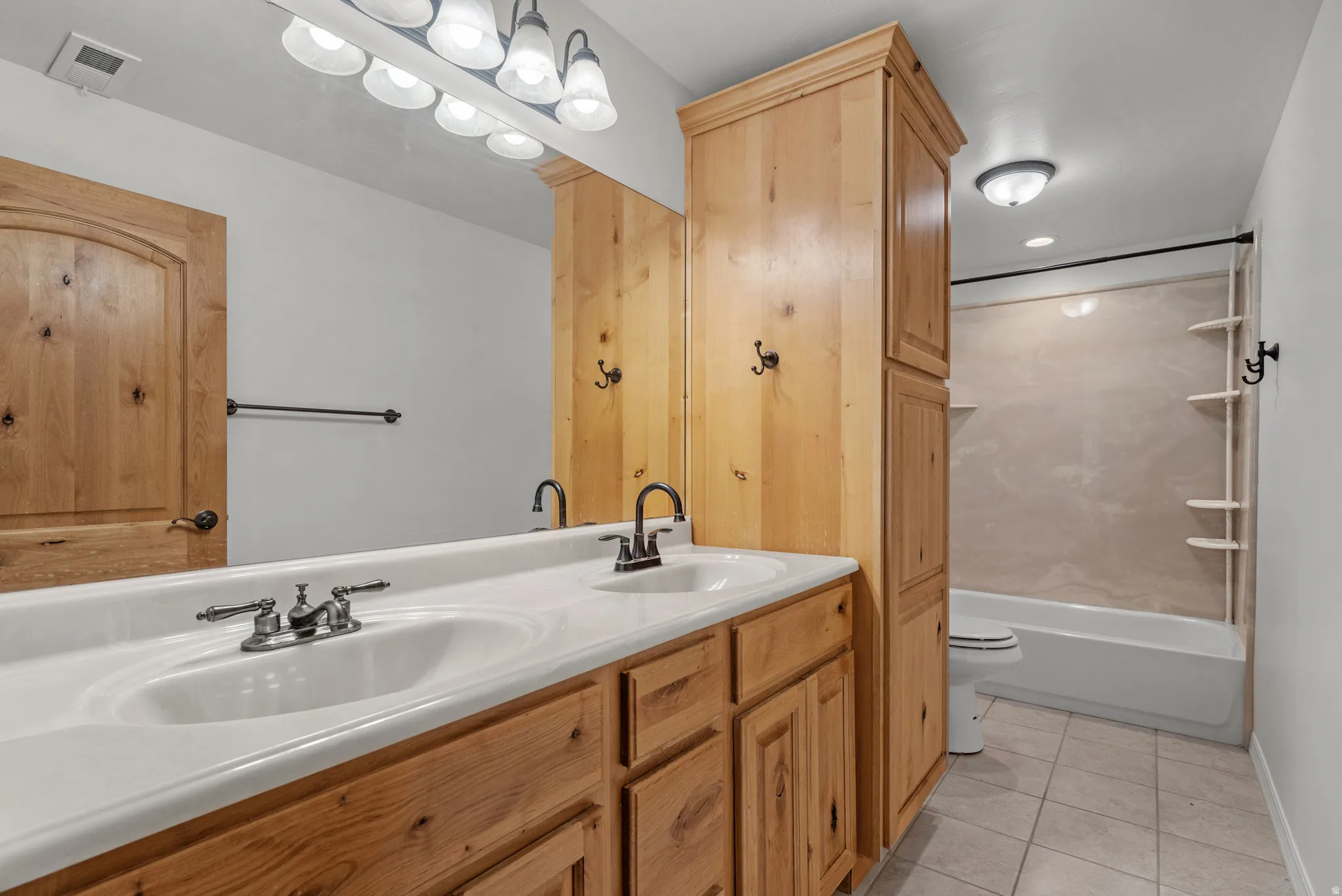 Bathroom featuring a double vanity with integrated sinks, wood-finish cabinetry, built-in storage tower, and a tub-shower combination with integrated shelving