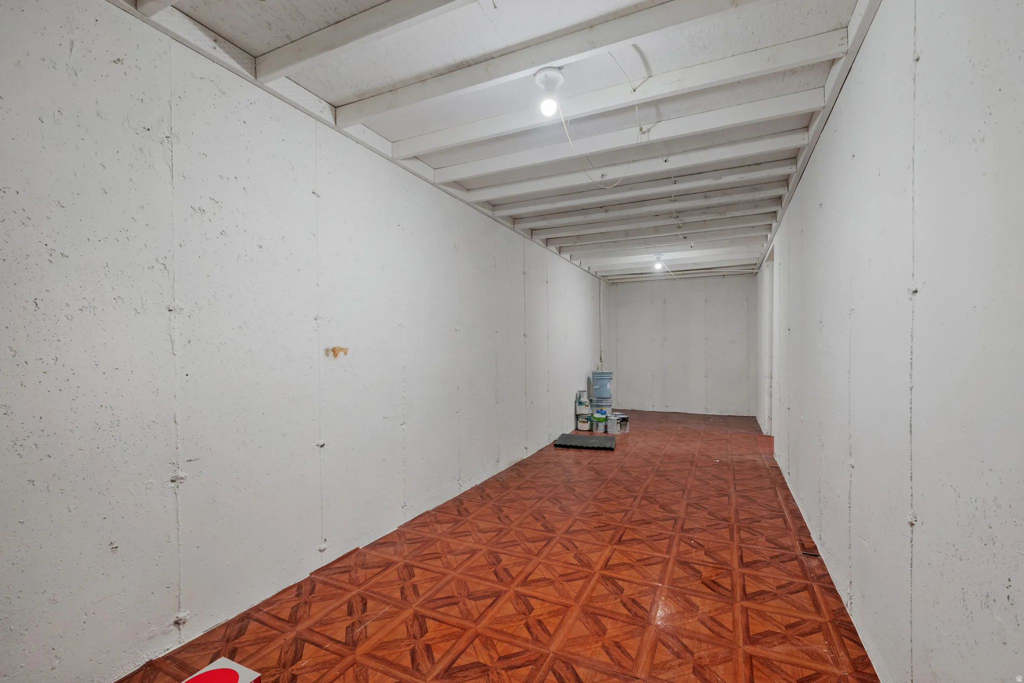 Finished basement area featuring patterned tile flooring, exposed ceiling joists, and white-painted walls