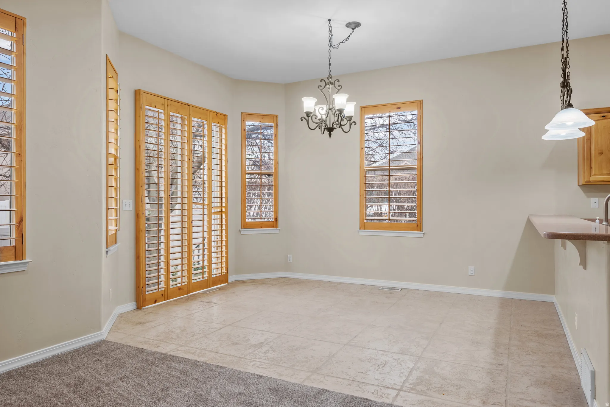Open-concept dining area featuring light-toned tile flooring, custom wood plantation shutters, and a decorative chandelier