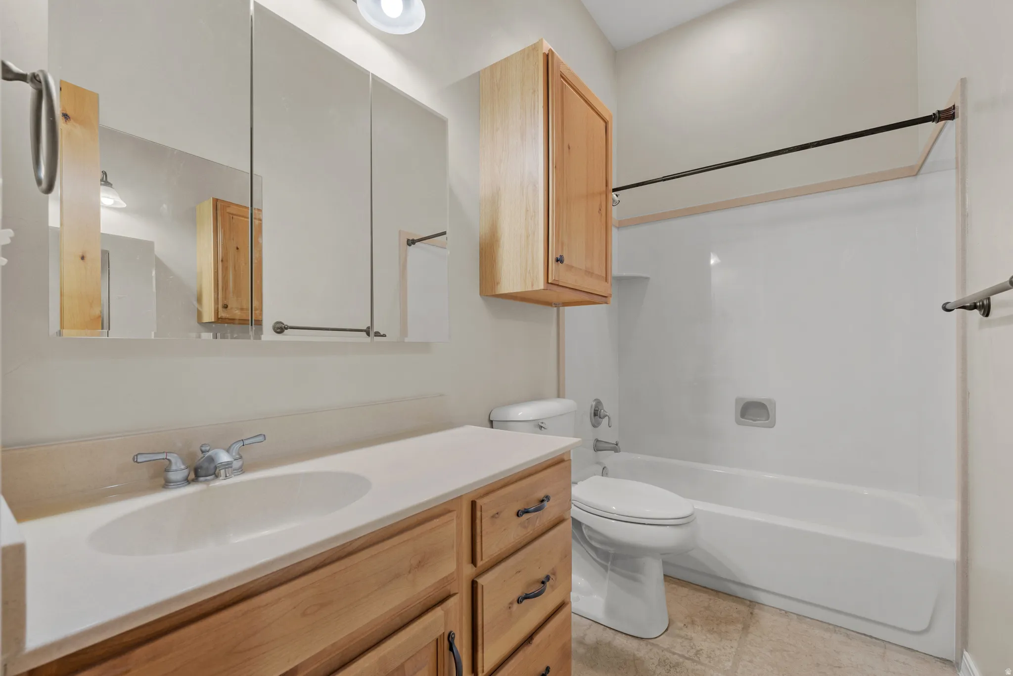 Bathroom featuring a wood-finish vanity with integrated sink, a large mirrored medicine cabinet, a full-size bathtub with shower capabilities, a toilet, and overhead lighting