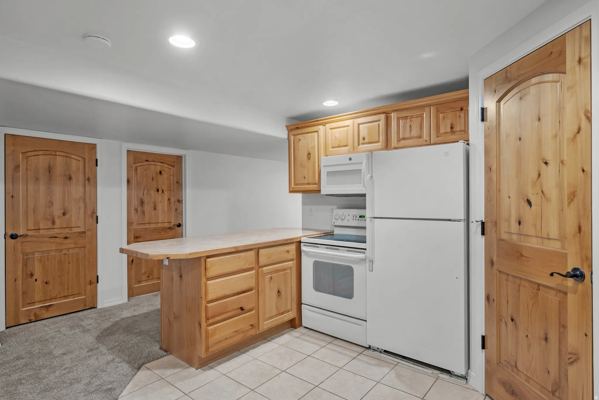 Compact kitchen space featuring white appliances, light wood-finish cabinetry, and a peninsula countertop