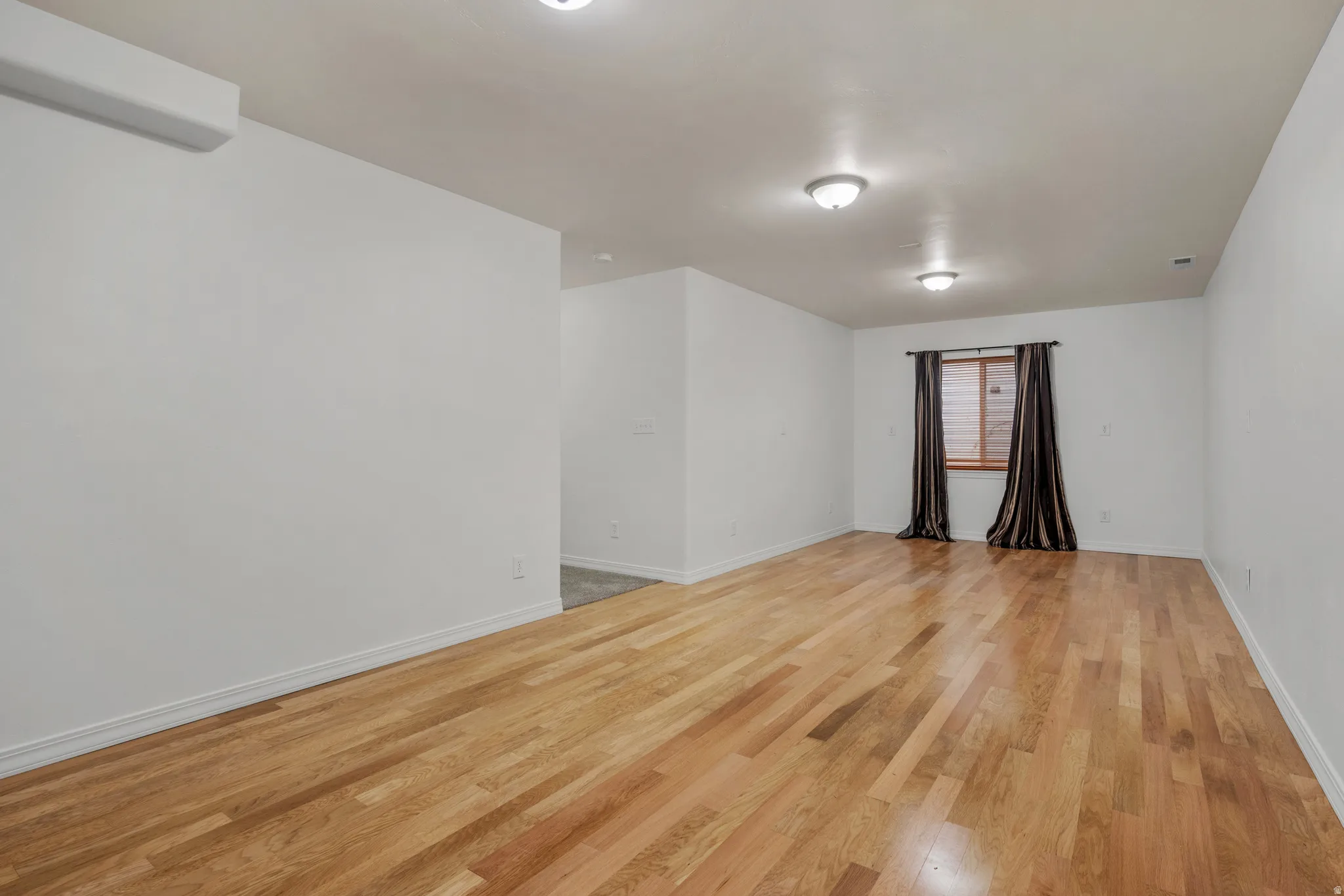 Spacious room featuring wood-finish flooring, recessed lighting, and a window with blinds and drapes