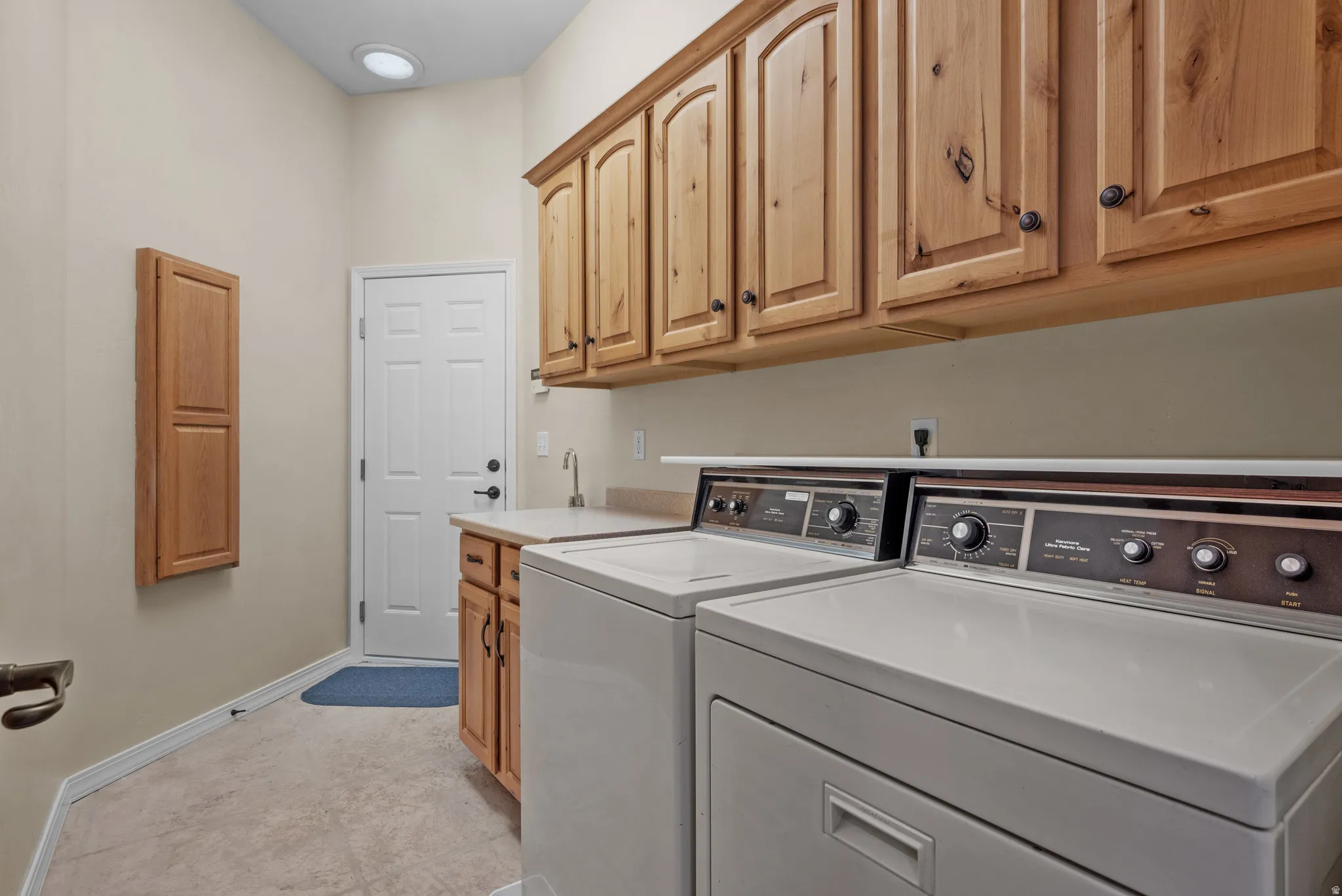 Laundry room featuring tiled flooring, extensive wood cabinetry, a utility sink, and a white six-panel door