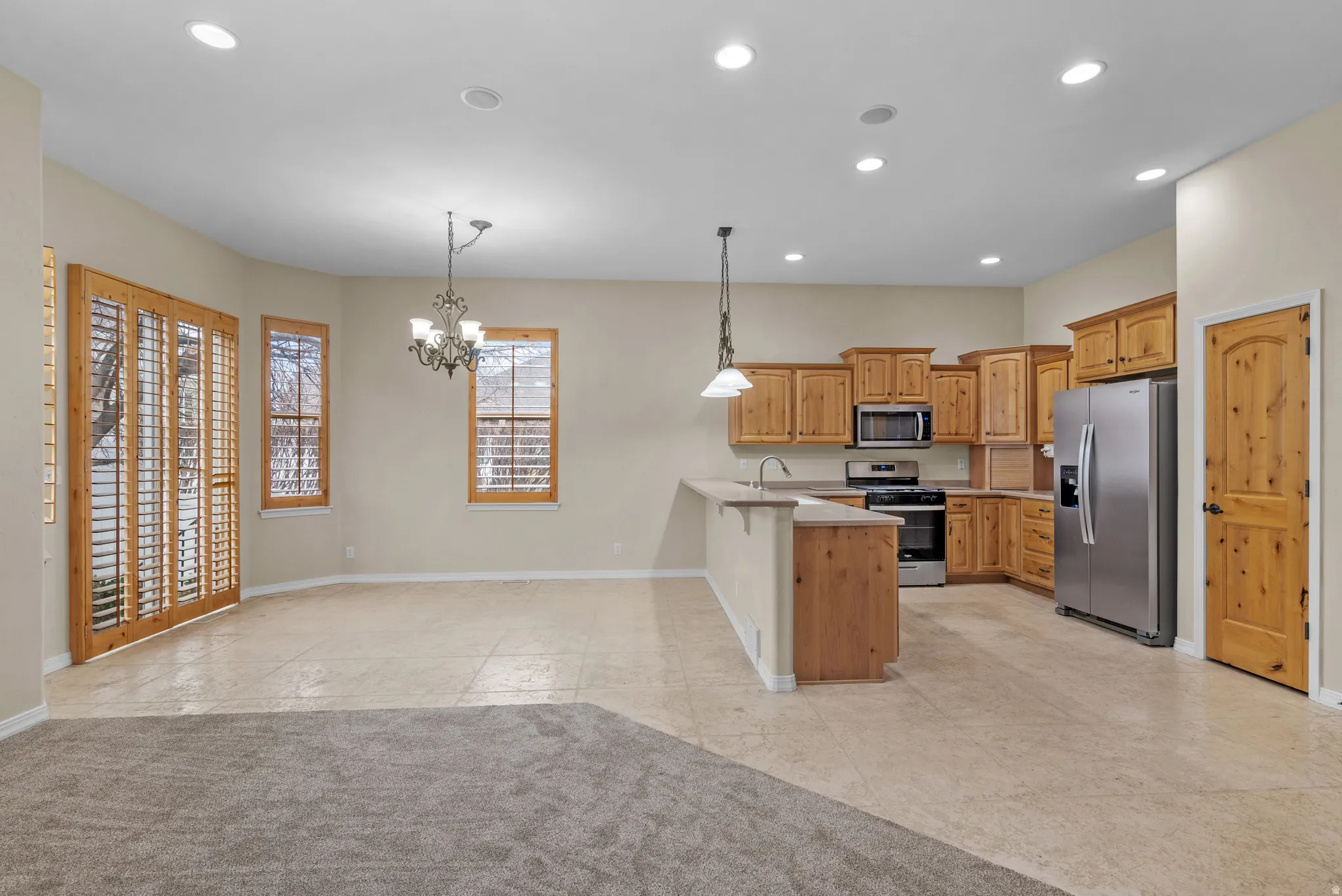 Open-concept kitchen and dining area featuring light wood cabinetry, stainless steel appliances, and a central island with a breakfast bar