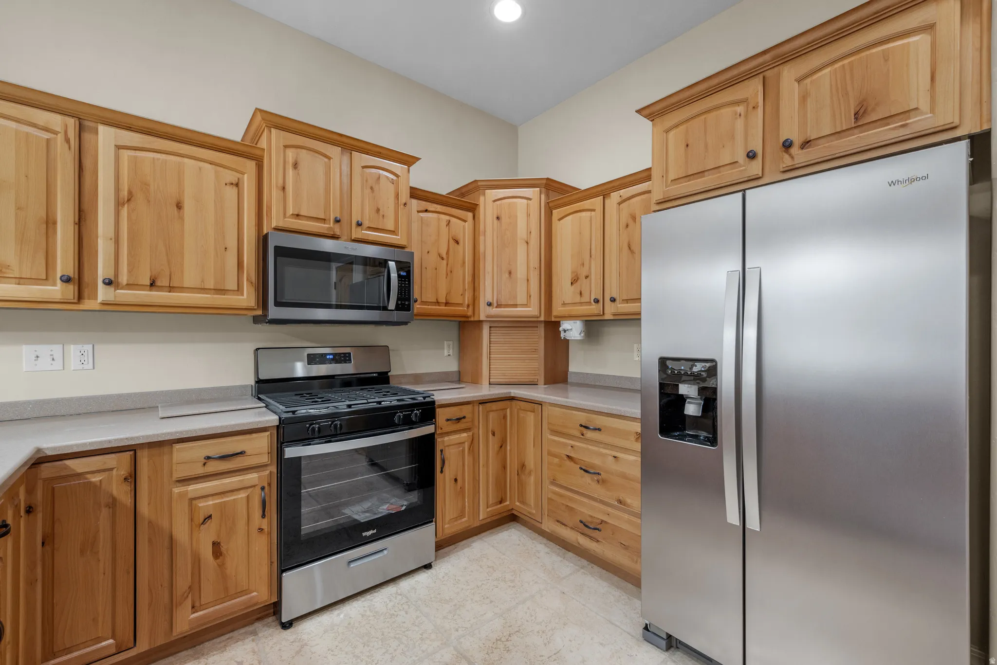 Kitchen featuring natural wood cabinetry, light-toned countertops, stainless steel appliances, and tile flooring