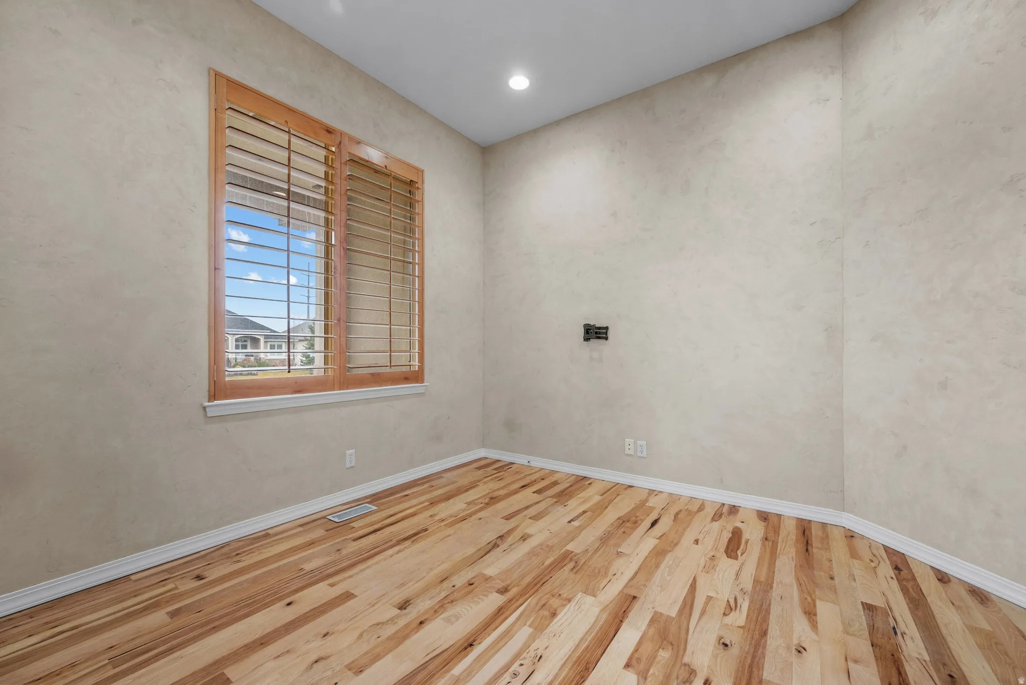 Room featuring wood-finish flooring, textured wall finish, and a window with wood plantation shutters
