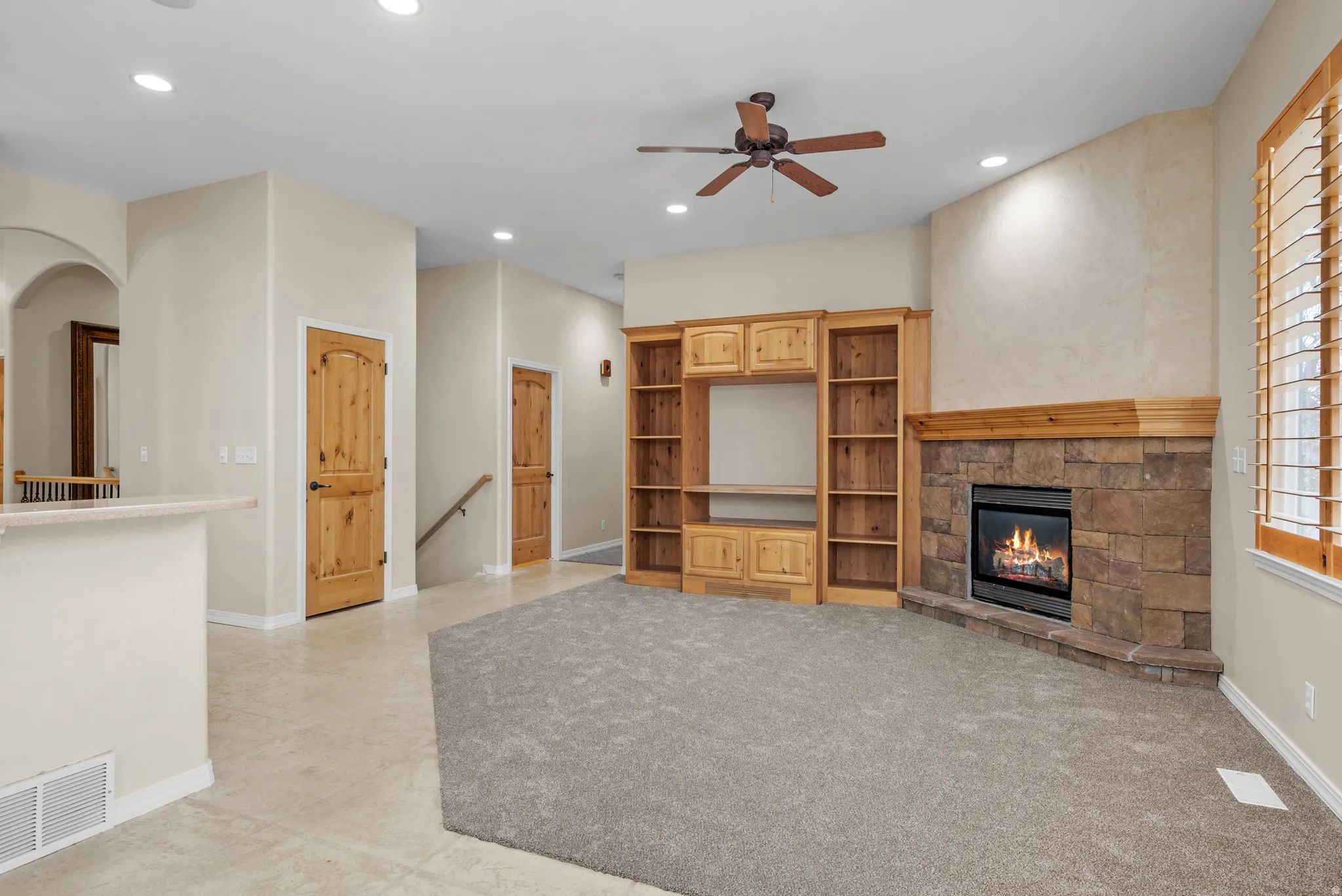 Living area featuring a stone fireplace with a wood mantel, built-in entertainment center, ceiling fan, and carpet flooring